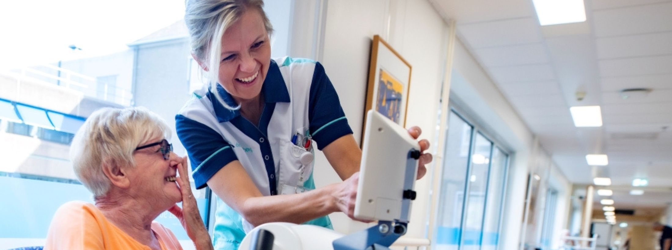 Cliënt en zorgmedewerker in de geriatrische revalidatie zitten in een uitleggesprek en lachen samen.