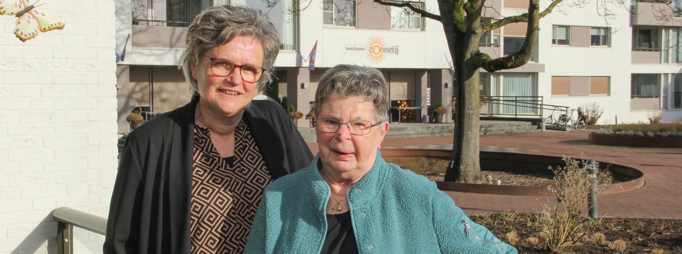 Welzijnscoach Gerrie van Bussel en bewoner Annemie staan naast elkaar buiten locatie Zonnetij.