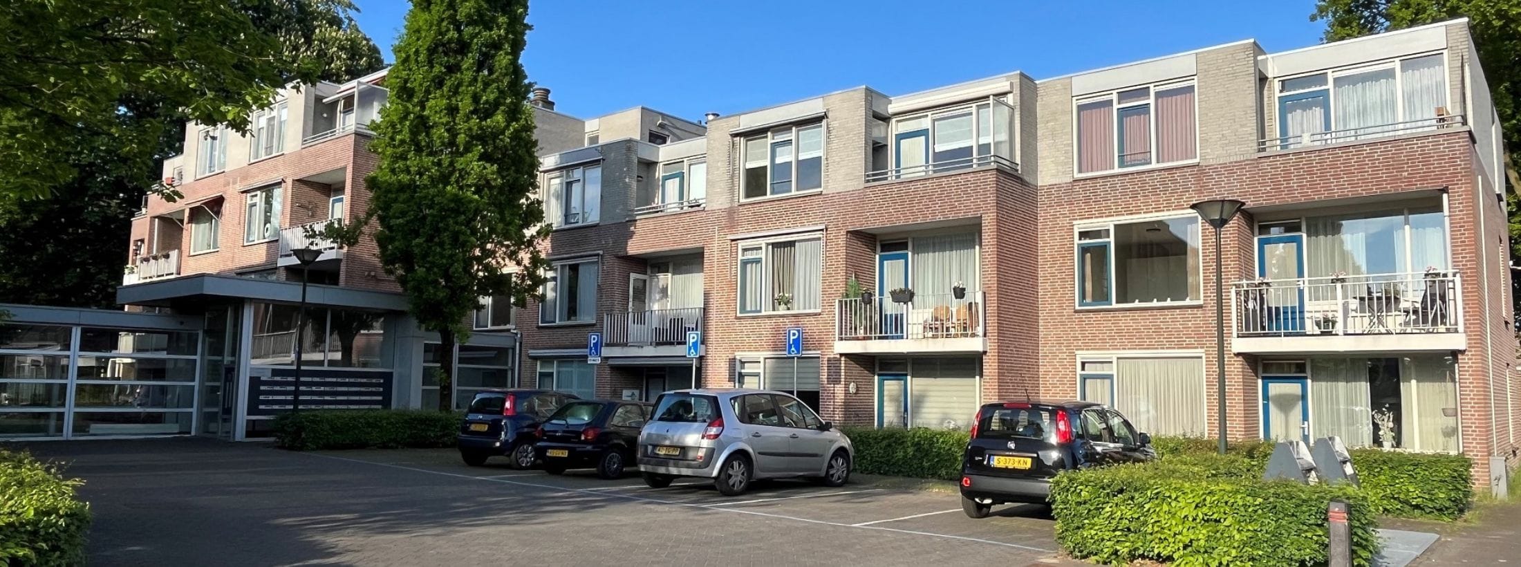 Buitenaanzicht van de Ireneflat van locatie Ruijschenberg met een parkeerplaats voor de ingang.