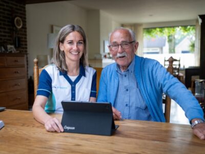 Een zorgmedewerker helpt een cliënt bij het gebruiken van een laptop.