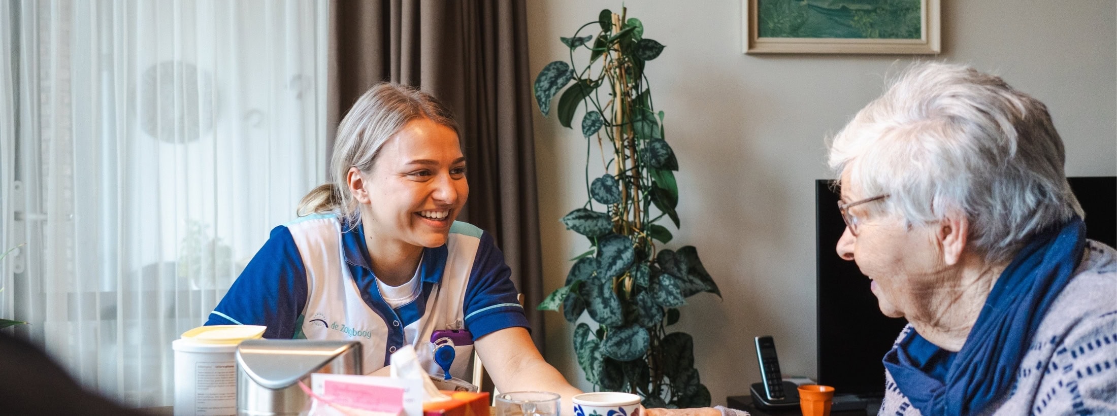 Zorgmedewerker en cliënt zitten samen aan de eettafel en zijn in gesprek.