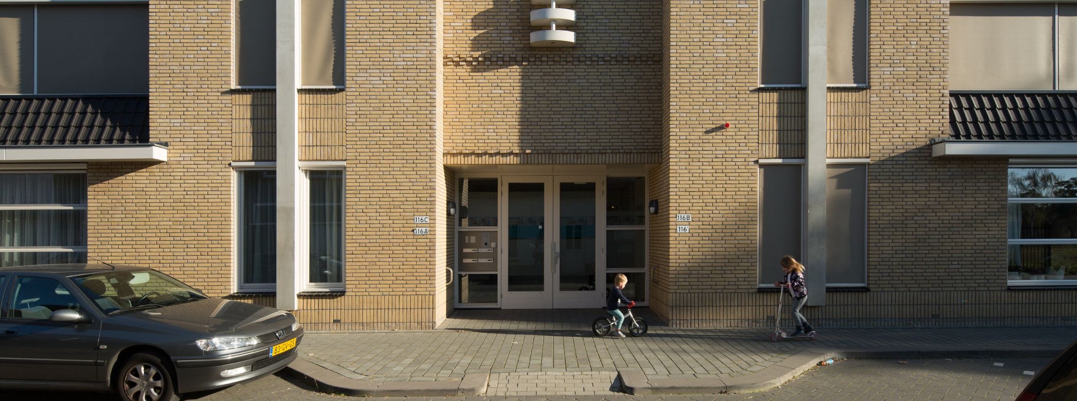 Buitenaanzicht van locatie Wolfstraat met twee kinderen bij de ingang, één op een fietsje en één op een stepje.