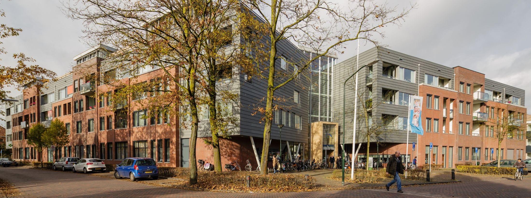 Buitenaanzicht van locatie Ruijschenberg met bomen, fietsen en auto's bij de ingang.