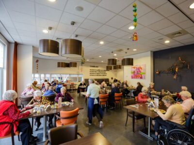 Cliënten zitten aan verschillende tafels terwijl cateringmedewerkers eten serveren.
