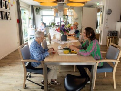 Cliënt en medewerker zitten tegenover elkaar aan tafel met fruit, in een gemeenschappelijke ruimte.