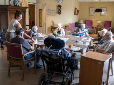 Cliënten zitten samen aan tafel en eten soep die door een medewerker wordt opgediend.
