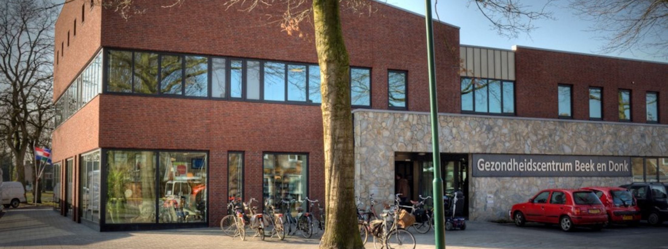 Buitenaanzicht van Medisch Centrum Beek en Donk met fietsen en auto's bij de ingang.