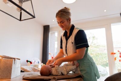 Een Zorgboog medewerker verzorgt een pasgeboren baby thuis op een tafel.