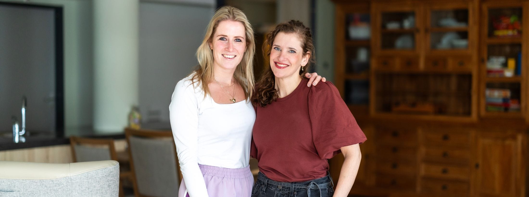 Twee casemanagers Parkinson poseren naast elkaar in een huiskamer.