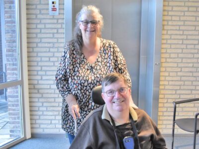 Portretfoto van transfervrijwilliger Carla van Neerven, staand achter cliënt in rolstoel.